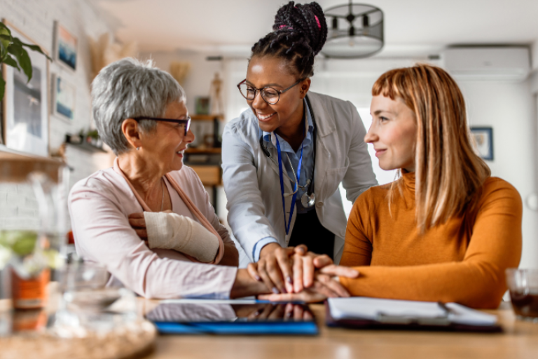 Three woman smiling at a desk in a home with clipboard in front of them 
