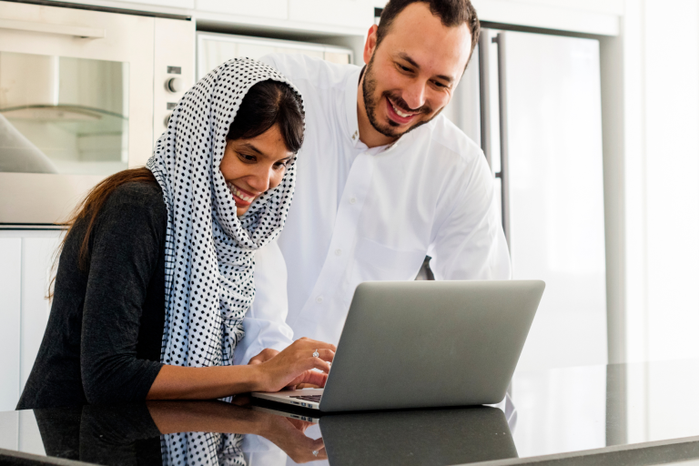Adult male and female looking at an open laptop in a kitchen