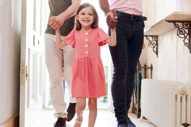 Young girl in pink dress walking into a hallway holding hands with two adults