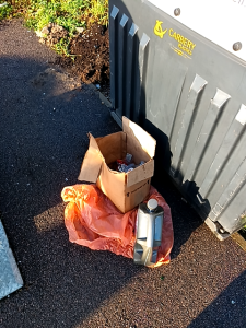Containers of waste oil in boxes and bags, fly-tipped outside a recycling bank 