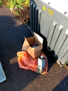 Containers of waste oil in boxes and bags, fly-tipped outside a recycling bank