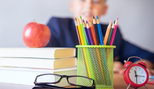 books, pencils, glasses, clock in front of school child