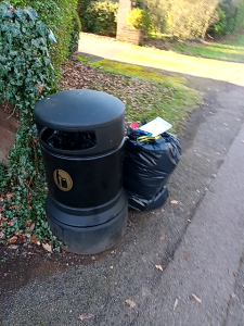A black bag of waste left next to a litter bin