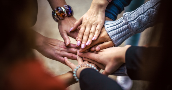People with their hands in the middle of a circle showing support for one another.