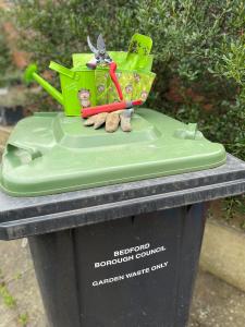 Green lidded bin with gardening tools on top