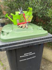Green lidded bin with gardening tools on top