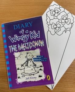 A copy of a Diary of a Wimpy Kid book placed on top of an example of a library craft. The craft is a piece of card with an outline of a flower bouquet that children can colour in.