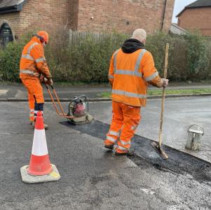 Two council workers repairing a pothole on a road in Bedford