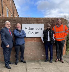 People standing next to a sign with 'Adamson Court' written on it