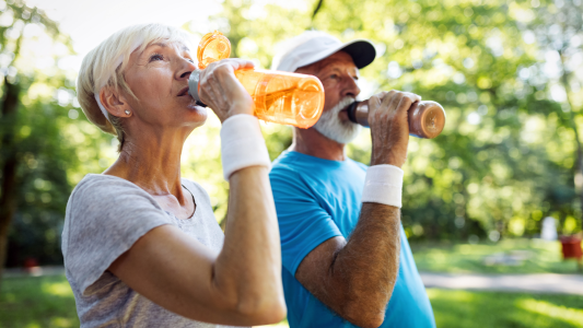 Man and woman outside drinking from their water bottles to stay hydrated.