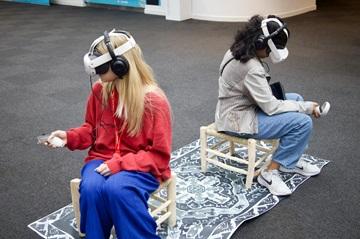 Two young people sitting, using VR headsets and controllers in their hand