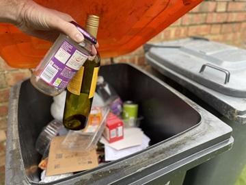 Glass bottle and jar going into an orange-lidded wheelie bin