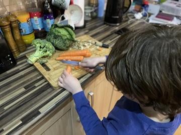 A child cutting vegetables on a chopping board with a knife