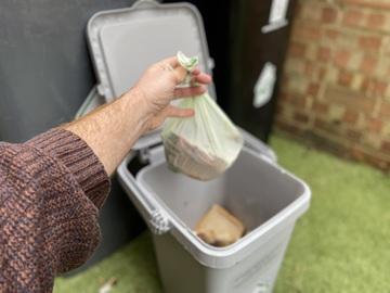 A bag of food waste being dropped in an outdoor food waste bin