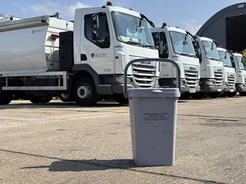 An outdoor food waste bin on the ground, in front of collection vehicles