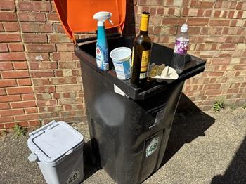 A food bin and orange-lidded recycling bin with a plastic spray and bottle, yoghurt pot, egg box and glass bottle