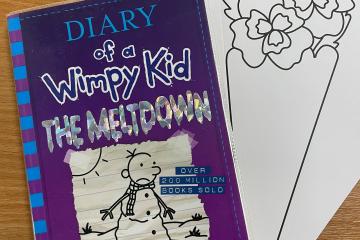 A copy of a Diary of a Wimpy Kid book placed on top of an example of a library craft. The craft is a piece of card with an outline of a flower bouquet that children can colour in.