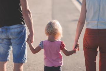 A child holding hands with two adults