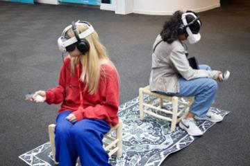 Two young people sitting, using VR headsets and controllers in their hand