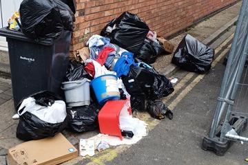 Fly-tipping in Bedford - an overflowing black bin surrounding by rubbish and black bags