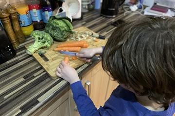A child cutting vegetables on a chopping board with a knife