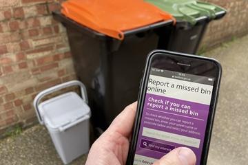 A mobile phone showing the missed bin webpage, with bins in the background