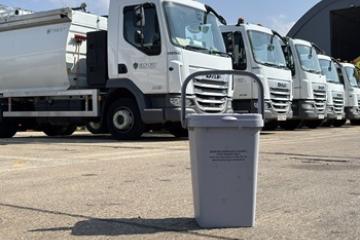 An outdoor food waste bin on the ground, in front of collection vehicles