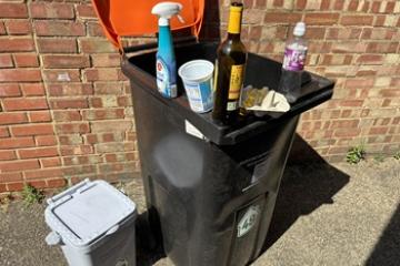 A food bin and orange-lidded recycling bin with a plastic spray and bottle, yoghurt pot, egg box and glass bottle