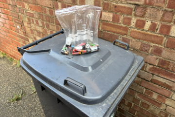 Sealed clear bag of batteries on a wheelie bin