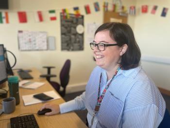 Female staff member at at desk and smiling at computer