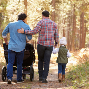 Two men walking together one pushing a buggy and one holding hands with a child 